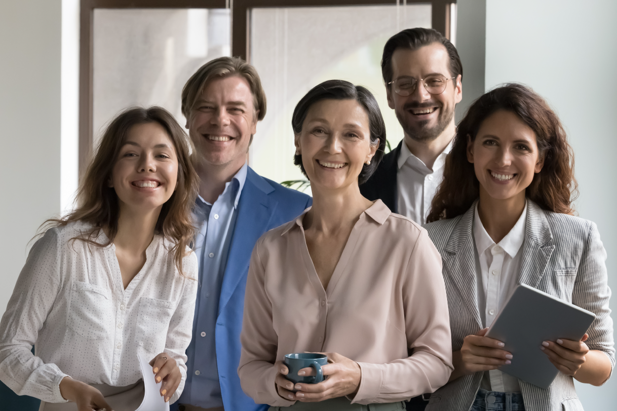 A group of adult women and men standing near a table smiling in an office