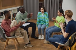 Counselor and young adults sitting in a support circle. All clapping hands after one kid shares their story.