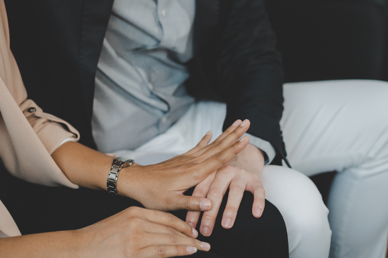 A man's hand on a woman's knee. Her hand is pushing his hand away.