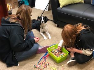 A counselor doing play therapy with a child on the floor with a therapy dog sitting beside them